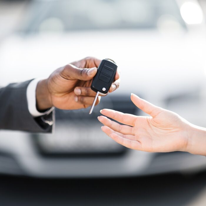 Car salesman handing over keys for new car to young woman