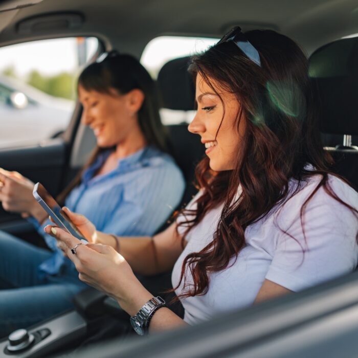 Side view of happy traveler girls sitting in car with cellphones.